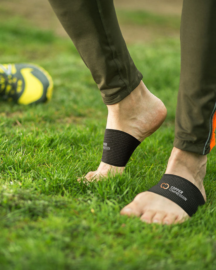Copper Compression Arch Support Sleeves, bare feet in black arch supports on a soccer pitch