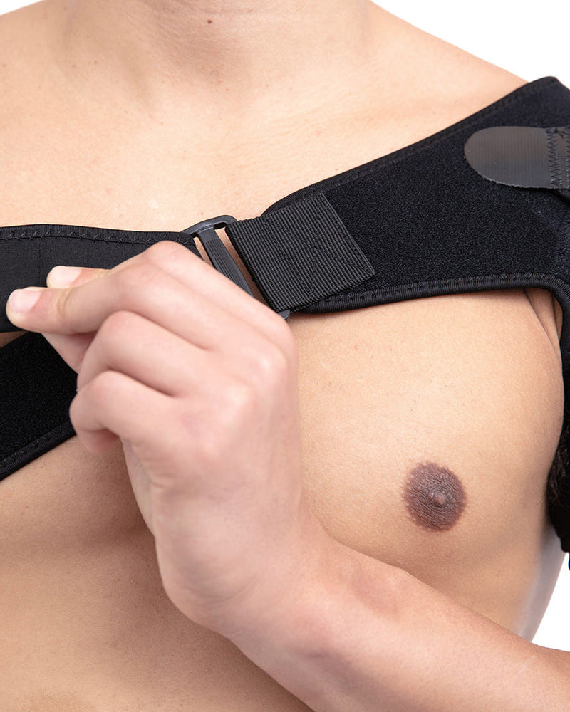 Copper Compression Shoulder Brace, a hand pulling the adjustment strap on the shoulder brace