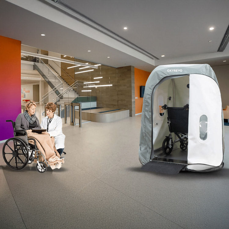 Two OxyRevo Heal40 chambers standing in a clinic corridor with staff and patients in wheelchairs nearby