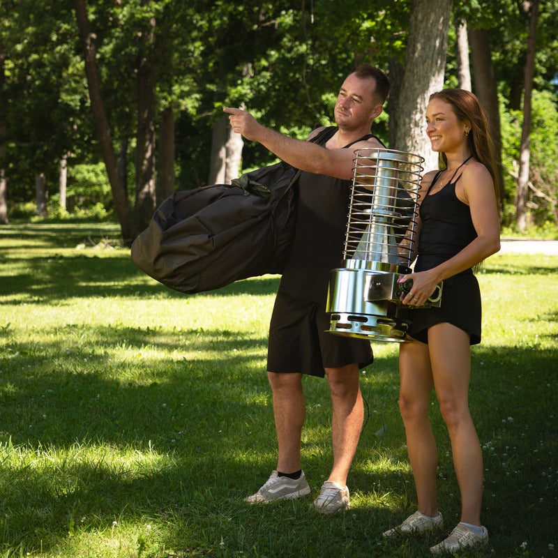 Two people carrying the packed tent bag and the gas heater across grass
