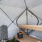 Tent interior with a bench and backrest along one wall and the heater's stone column at the end