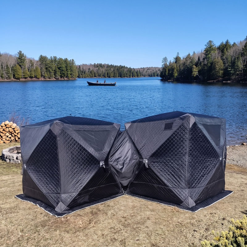Two black cube tents joined corner to corner beside a lake
