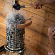Hands pouring water on the stones with the guard fitted, steam rising