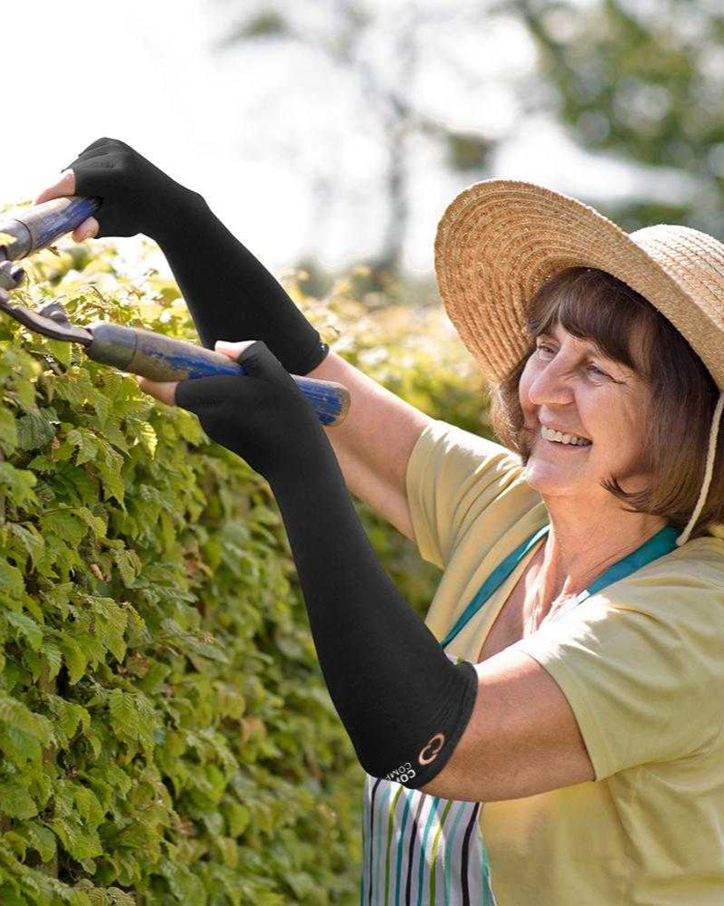 Copper Compression Long Arthritis Gloves, an older woman reaching up in a garden while wearing the long gloves
