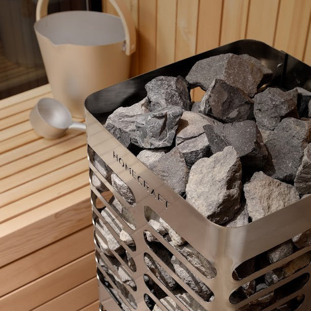 Homecraft Revive sauna heater filled with stones next to a sauna bucket