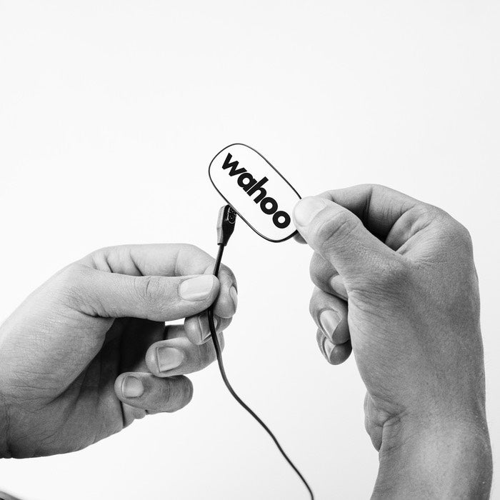 Wahoo TRACKR HEART RATE, hands holding the white pod with charging cable